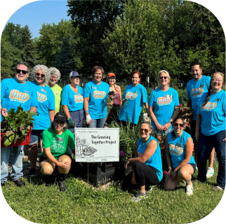 50 Shape Group of volunteers in matching blue shirts participating in 'The Growing Together Project,' supporting a community gardening initiative.