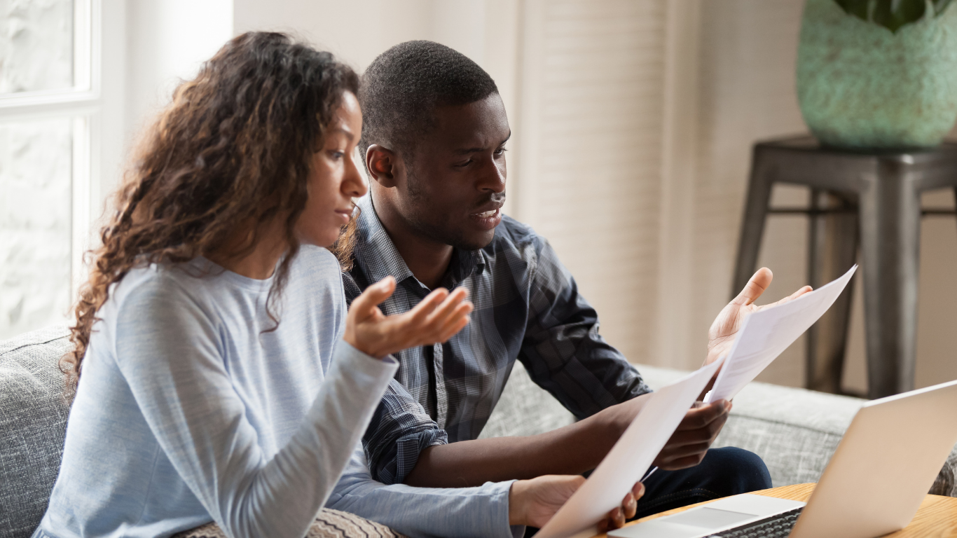 Concerned couple reviewing financial documents at home, discussing mortgage payments and household expenses.