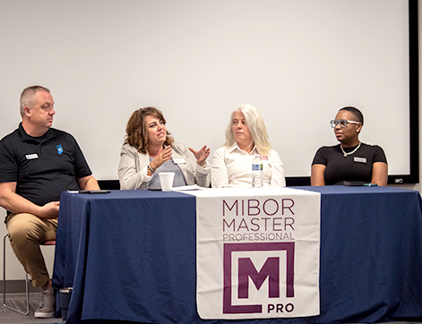 Secondary Header - MPRO Confident female speaker giving a presentation at a conference, standing at a podium with a laptop.